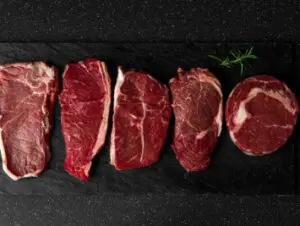 Five raw beef steaks on black background.